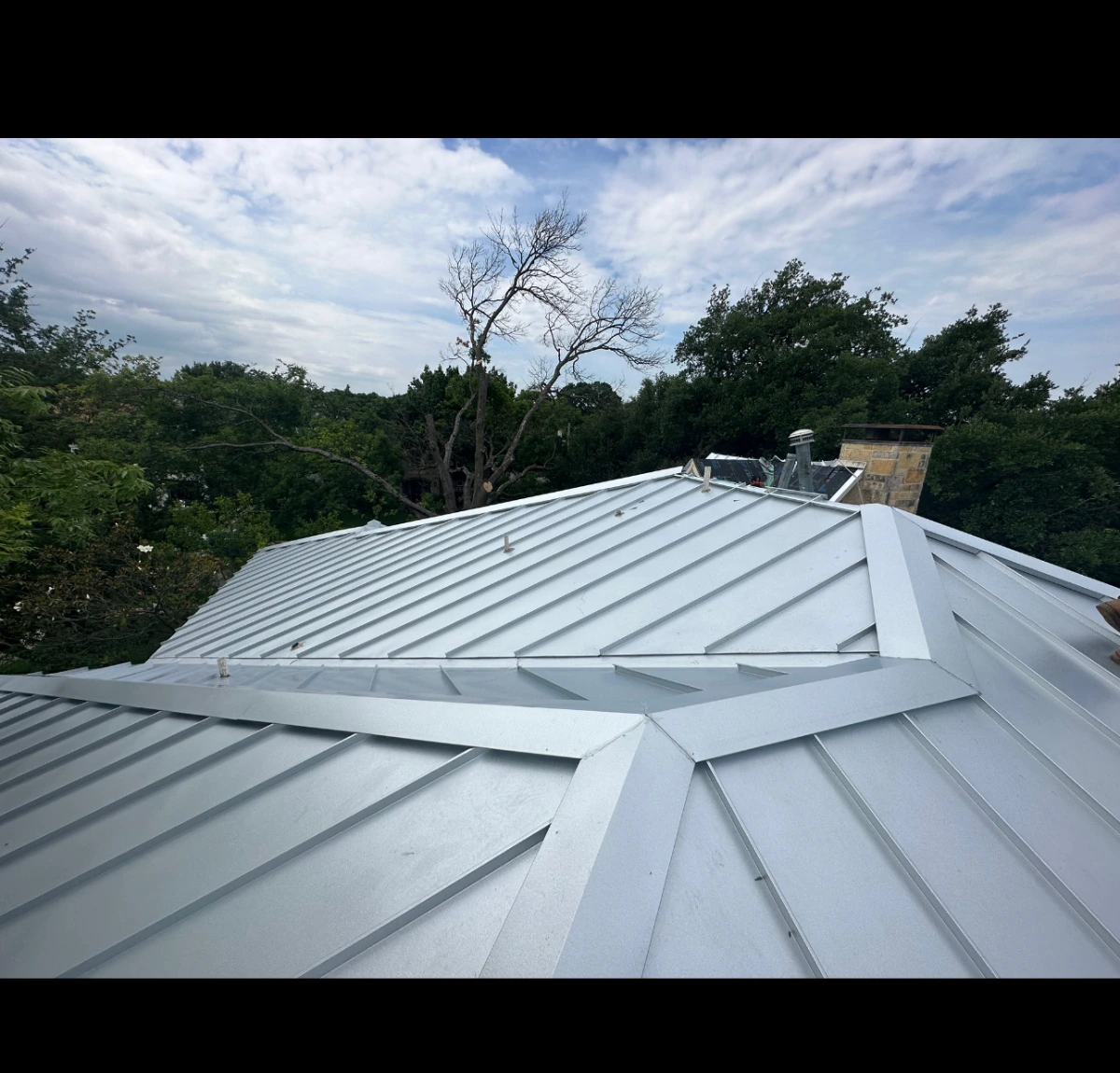 Standing seam metal roof installation with complex valleys and ridges on a Richardson, TX home with stone chimney