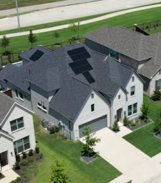Aerial view of a residential home in Prosper, TX with a newly installed rooftop solar panel system on a dark shingle roof, surrounded by neighboring homes and green lawns