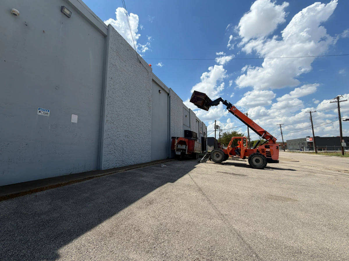 Telehandler staging materials beside a commercial building during a roof replacement in Dallas, Dallas County, TX.
