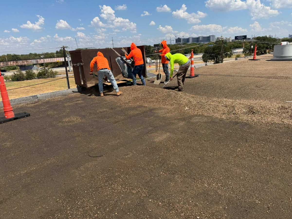 Under One Roof crew shoveling gravel off an existing built-up roof during a commercial roof replacement in Dallas, Dallas County, TX.