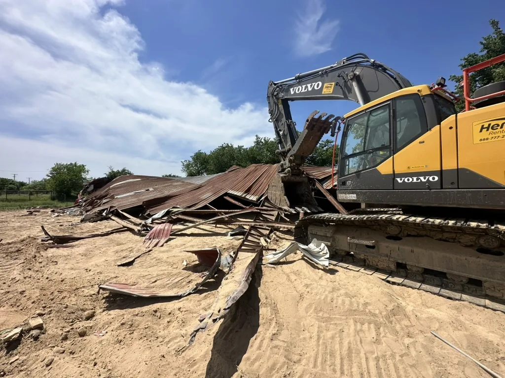 Excavator on a sand pad beside building debris during a building demolition