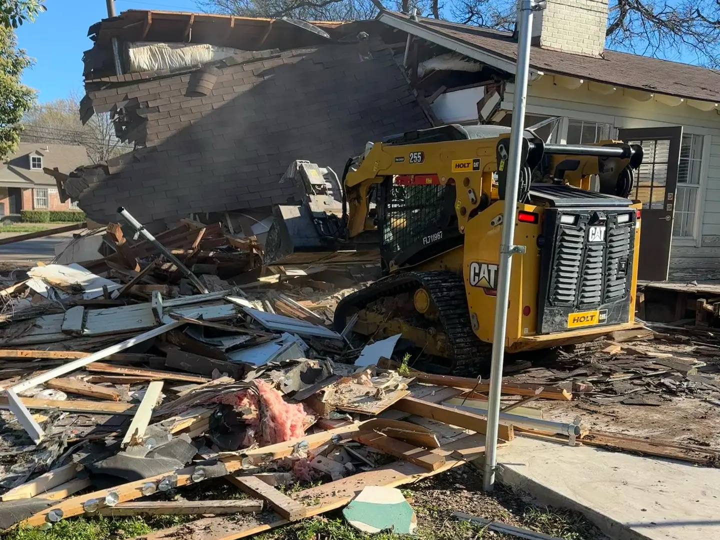 Skid steer clearing debris as a brick ranch house comes down during a house demolition