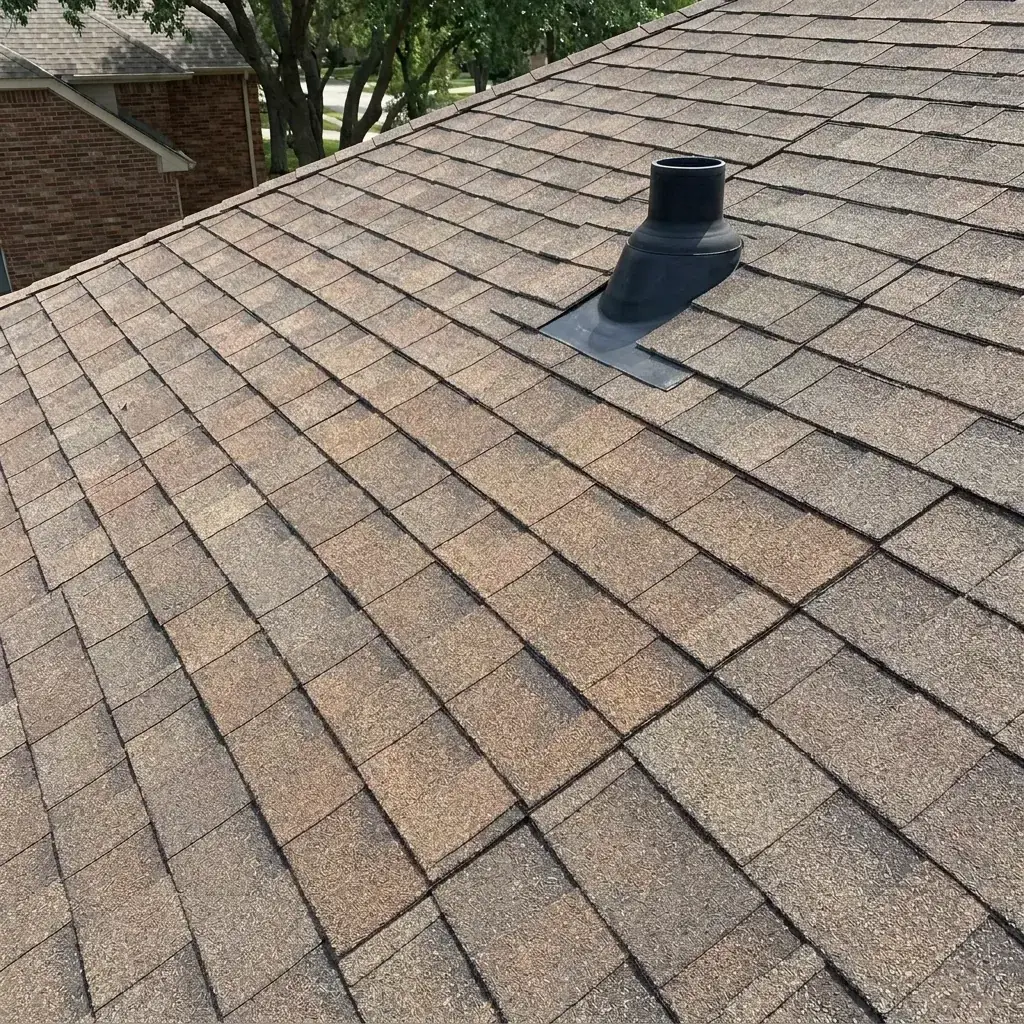 Close-up of a finished shingle repair around a plumbing vent boot, with replacement shingles matching the weathered architectural asphalt roof on a Farmers Branch home