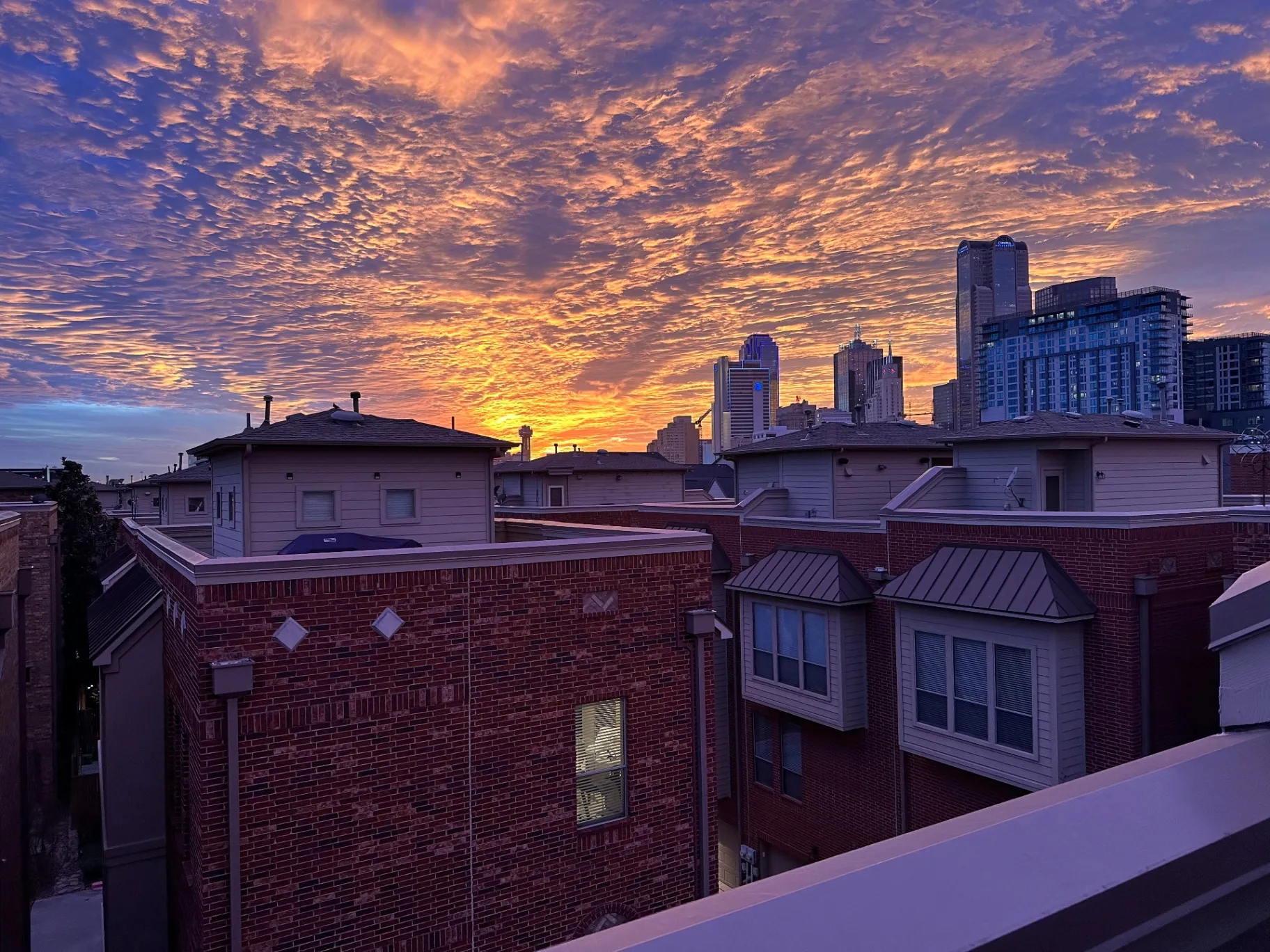 Beautiful sunset view over completed multi-unit residential roofing projects in Dallas, Texas, showing various roof types and styles with Dallas skyline backdrop