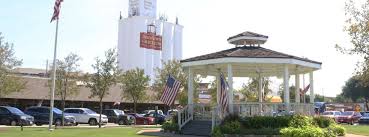 Carrollton Texas town square with historic gazebo and families enjoying community gathering space, children playing on green lawn with modern city buildings in background - Under One Roof roofing and home services coverage area