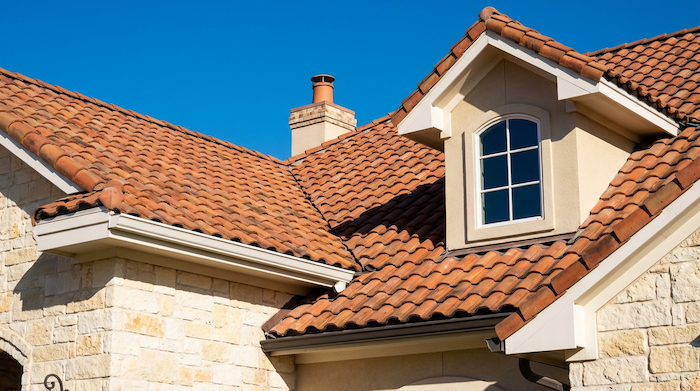 Clay tile roof installation on luxury home in Dallas, TX showing terracotta barrel tiles and chimney detail
